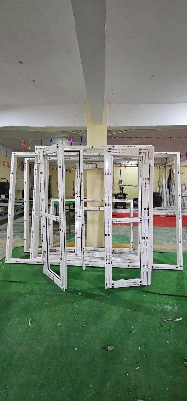A group of welded uPVC casement frames and sashes standing upright on a workshop floor