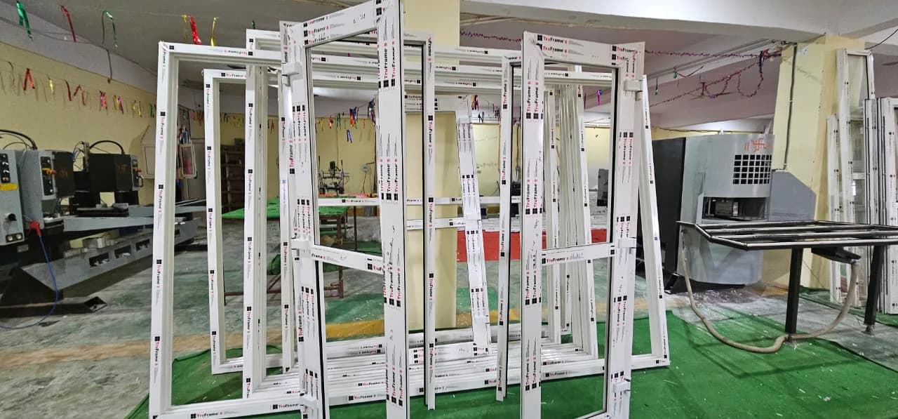 Welded white uPVC window and door frames, still in printed protective film, standing beside fabrication machinery