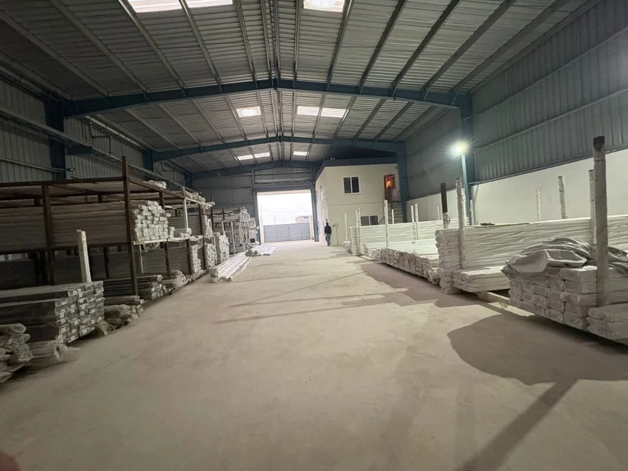 Long racks of white uPVC profile lengths stacked along both sides of a steel-roofed warehouse