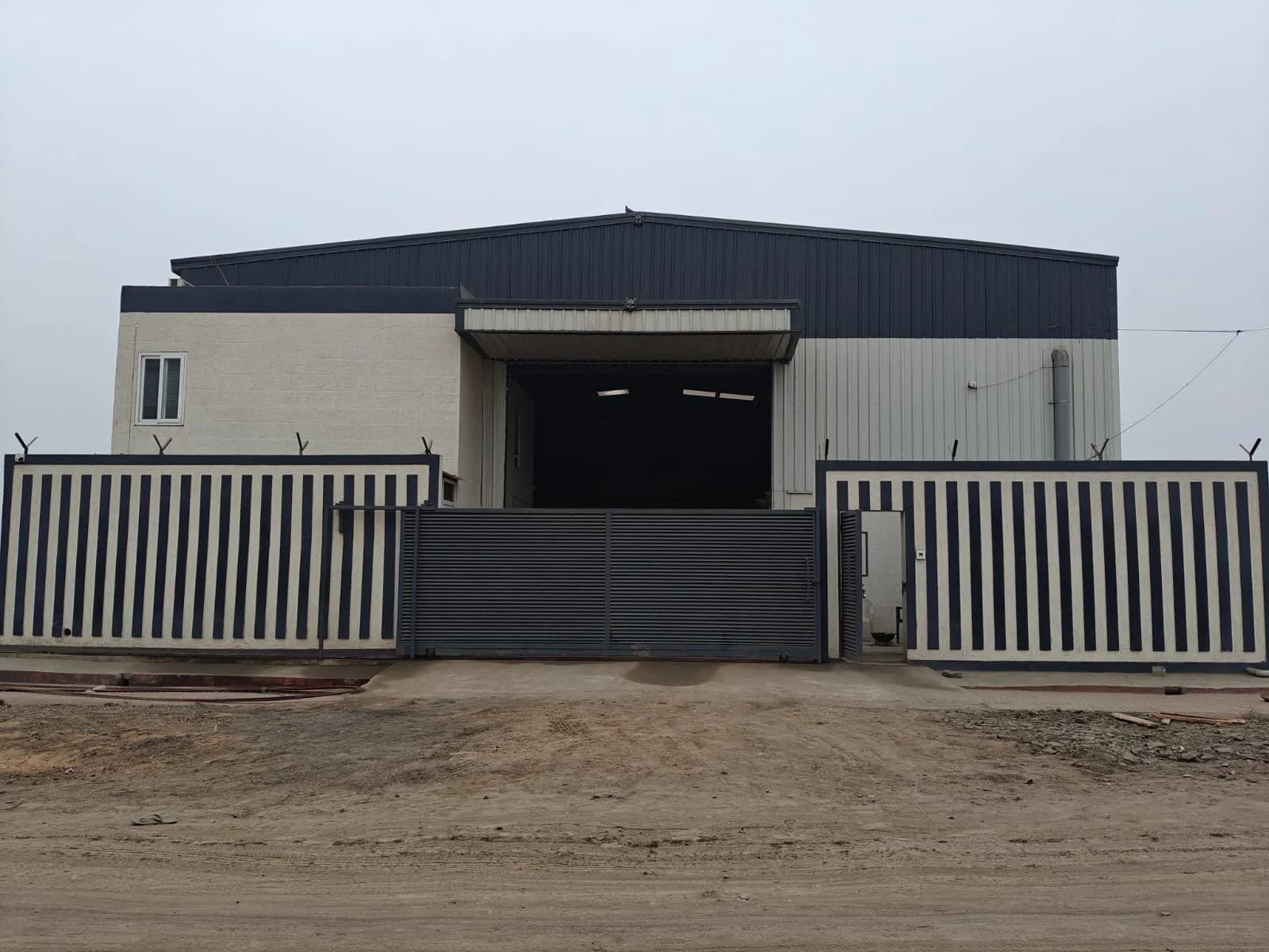 Exterior of an industrial shed with a steel roof and a striped boundary gate