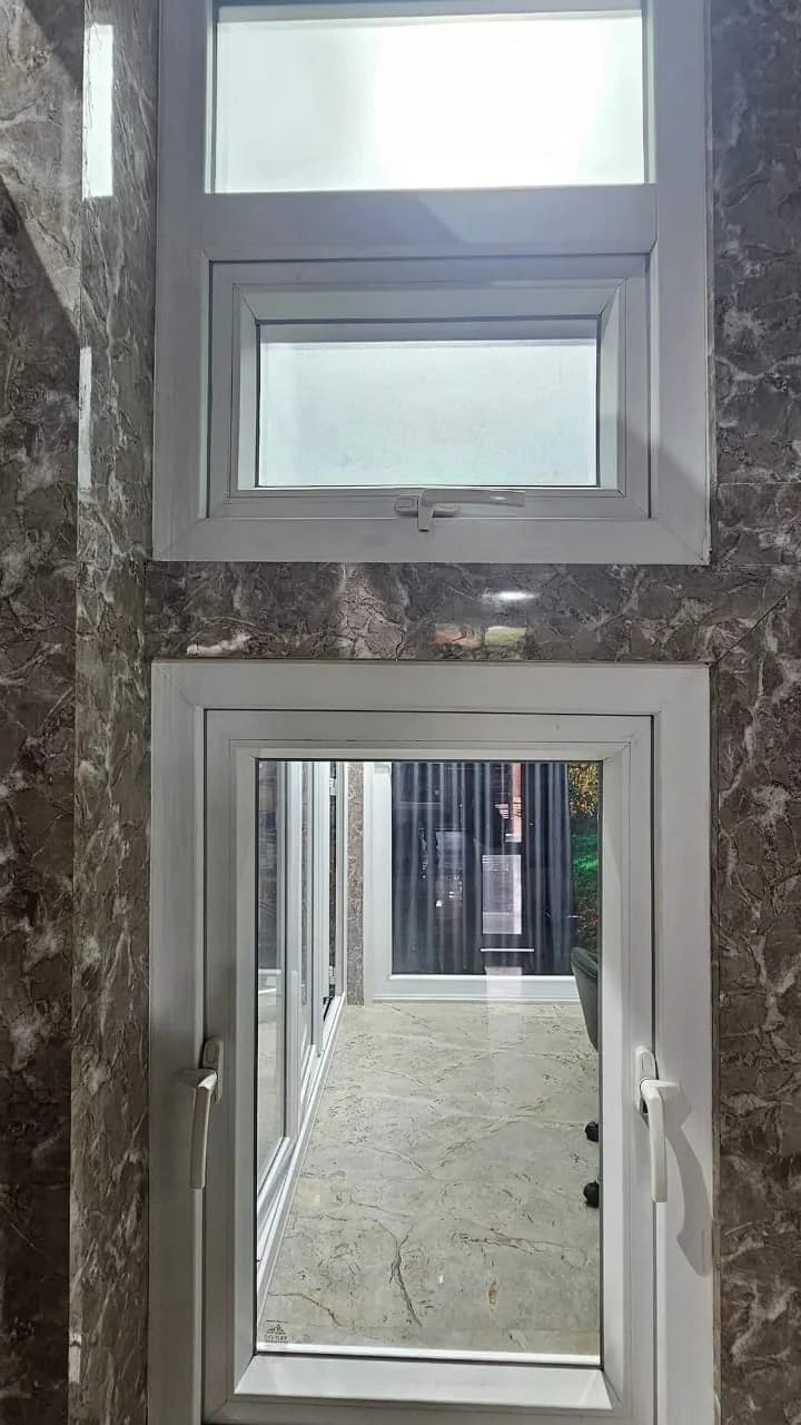 A white uPVC top-hung ventilator above a side-hung casement, set in a stone-clad display wall