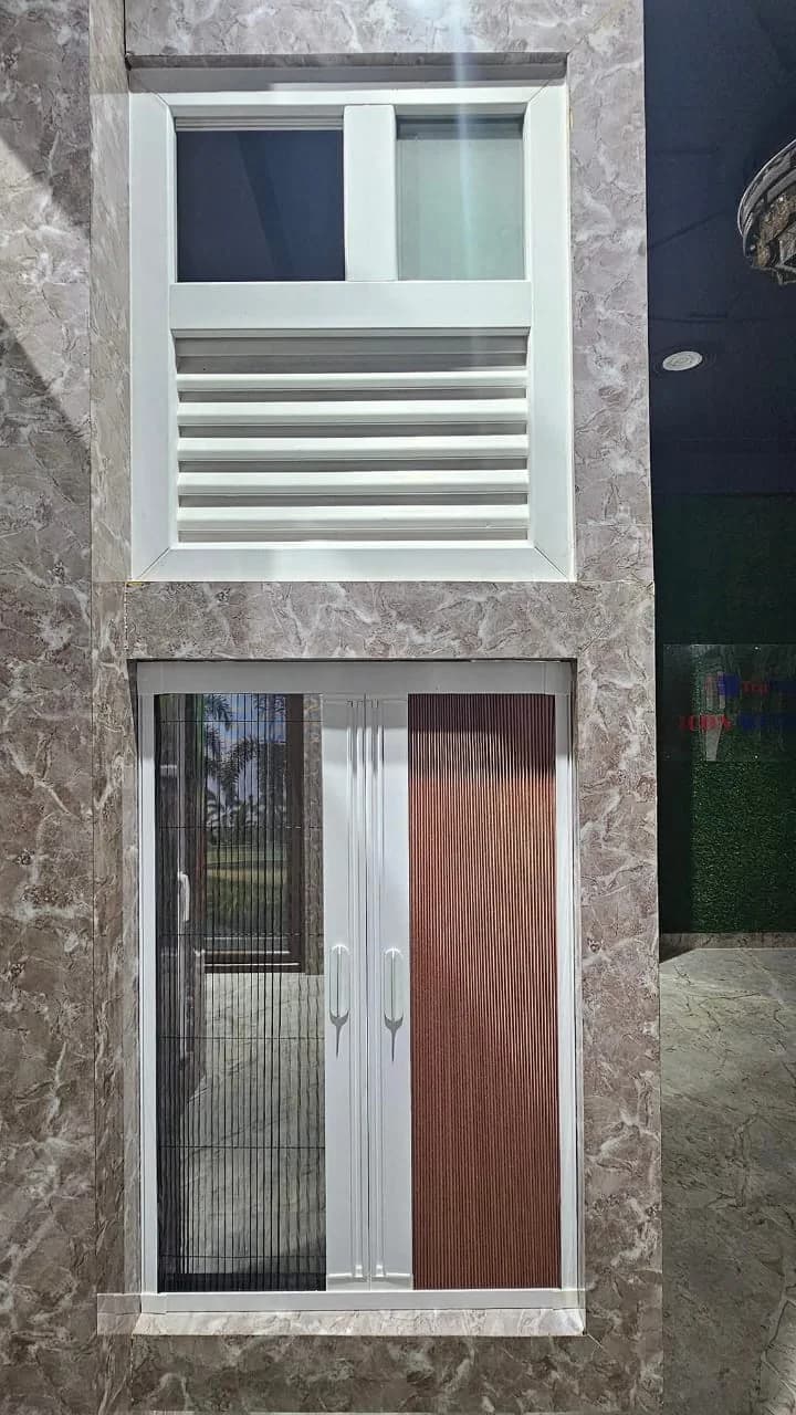 A white uPVC louvred ventilator above a double door with pleated insect mesh on one leaf and a wood-effect panel on the other